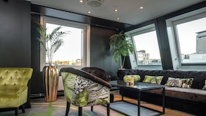 Eine moderne Lounge mit einer Couch, einem Sessel, einem Couchtisch, großen Fenstern und einer Zimmerpflanze.