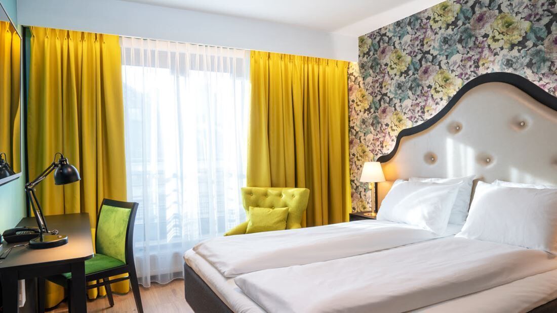 A hotel room with a bed, a desk, a chair, and a lamp.