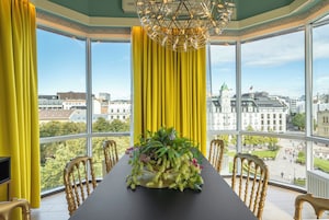 A room with a large window, a table with chairs, and a chandelier.