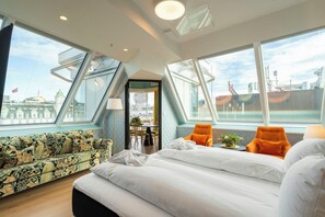 A modern hotel room with a large bed, two orange armchairs, a patterned sofa, and large windows offering a city view. - Thon Hotel Cecil (Oslo)