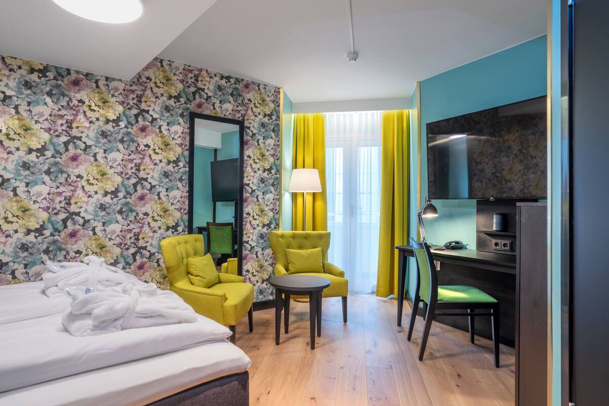A hotel room with a bed, a desk, a chair, a TV, and a mirror.
