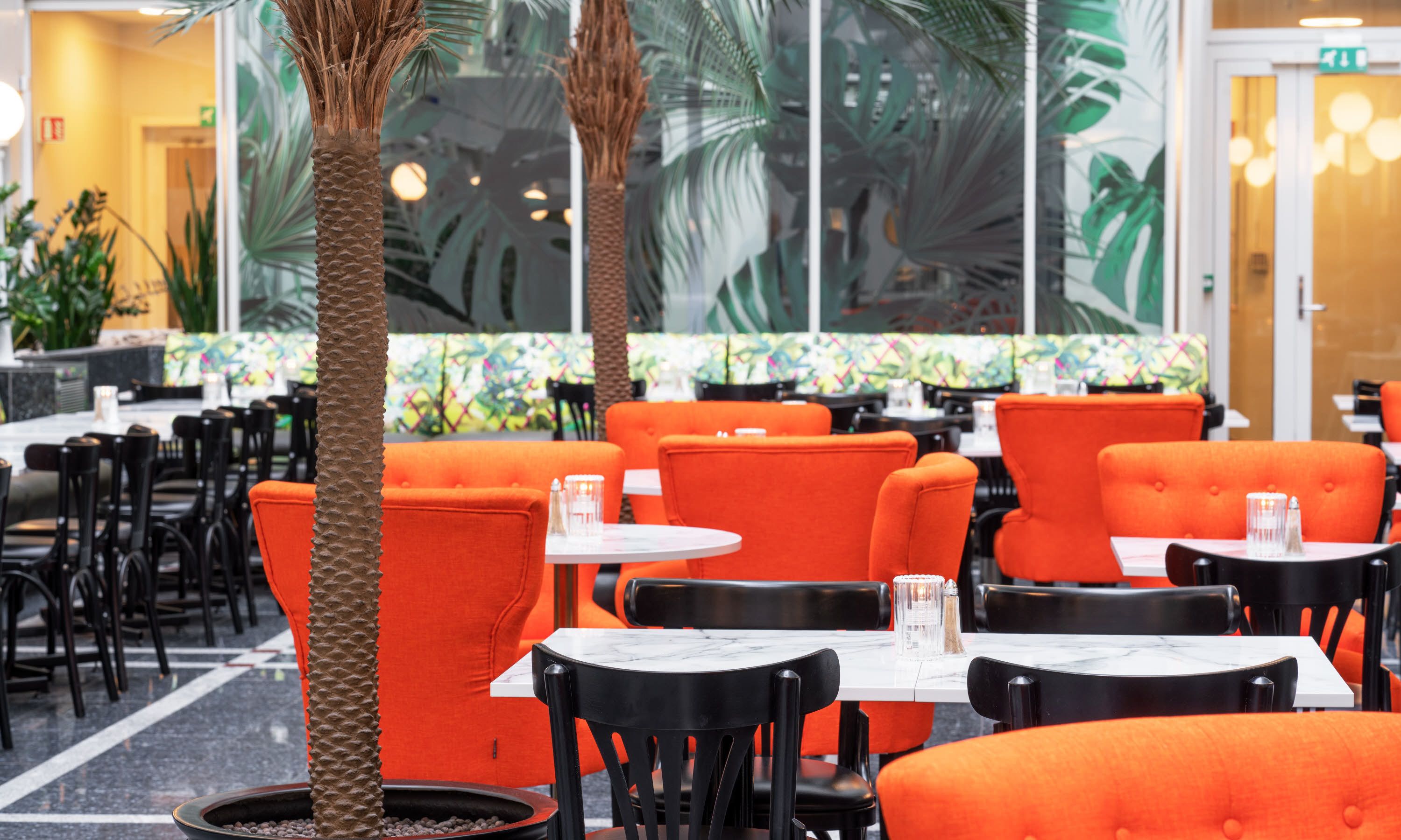 A restaurant with orange booths and black chairs, a marble-topped table, and a decorative wall with plant motifs.