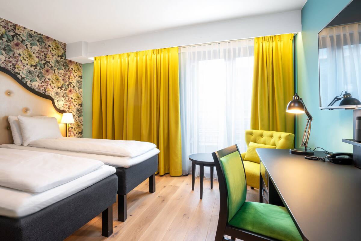A hotel room with two beds, a desk, a chair, a lamp, and a television.