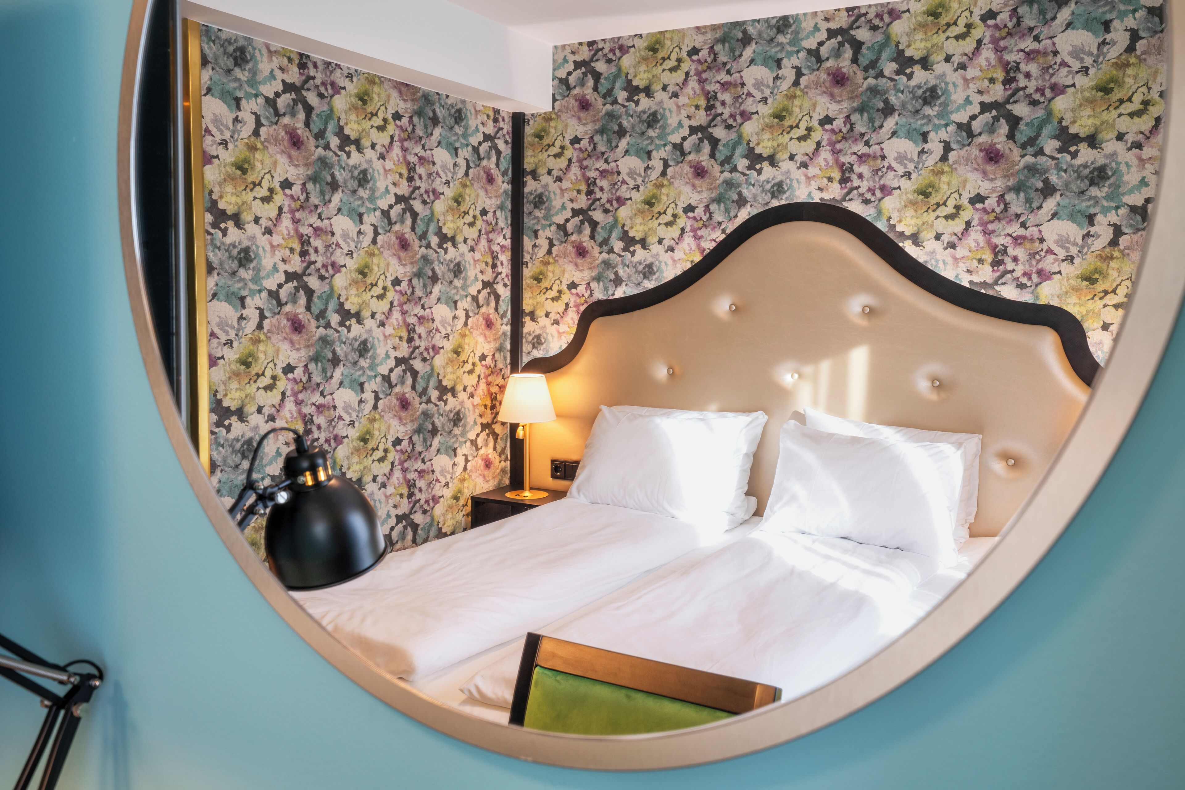 Une pièce circulaire comprenant un lit, une table de chevet, une lampe et un papier peint à motifs floraux.