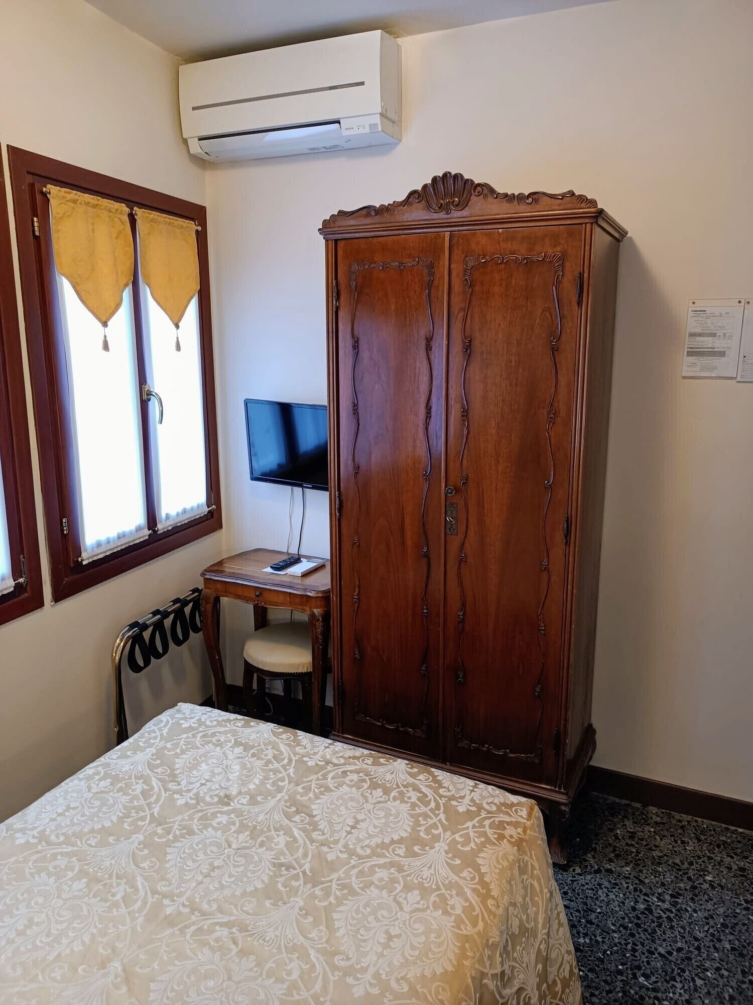 Ein Schlafzimmer mit einem Bett, einem Holzschrank, einem Schreibtisch mit Computer und einer Klimaanlage.