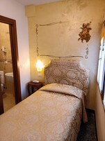 Quarto com cama, mesa de cabeceira, luminária na parede e um objeto decorativo na parede.