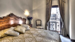 A bedroom with a large bed, a chair, a nightstand with a vase, and a view of a balcony with buildings. - Hotel Scandinavia - Relais (Venice)