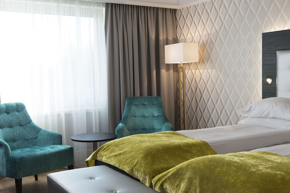 A hotel room with a bed, two armchairs, a small table, and a lamp.