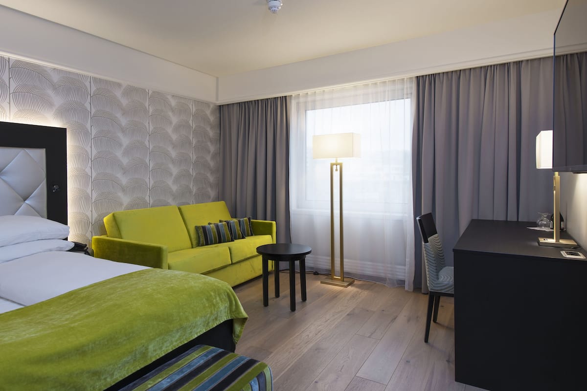 A hotel room with a large bed, a green sofa, a desk, and a floor lamp.