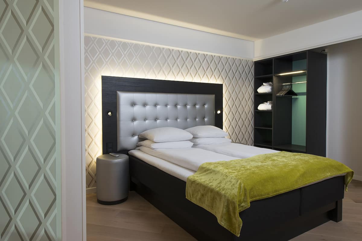 A modern bedroom with a tufted headboard, a bedside table, a trash bin, and a green throw blanket.