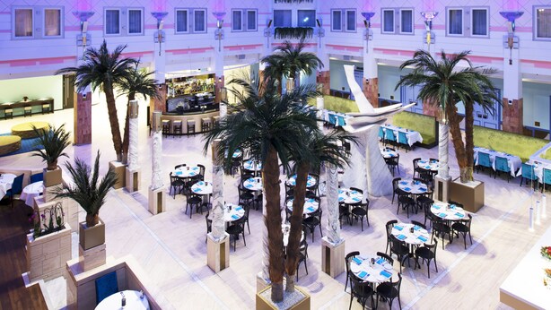 Un vaste atrium intérieur doté de plusieurs espaces de restauration, de palmiers et d’un haut plafond orné d’un motif étoilé.