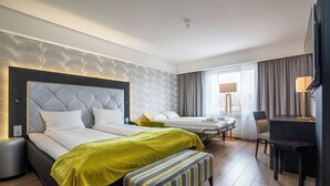 Une chambre d’hôtel avec deux lits, un bureau, une chaise, un banc, une télévision et une fenêtre avec des rideaux.
