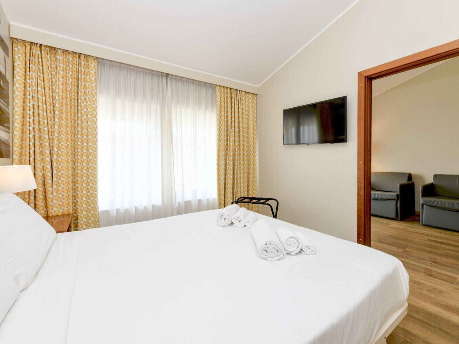 Habitación de hotel con cama, televisor montado en la pared y zona de estar con dos sillones.