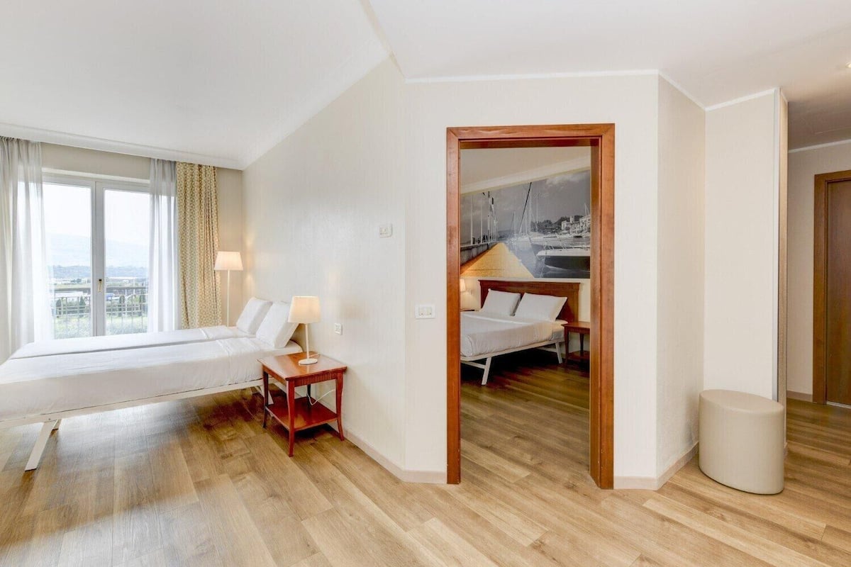 Une chambre d’hôtel avec une grande fenêtre, un lit, une table de chevet et une vue sur un port de plaisance.