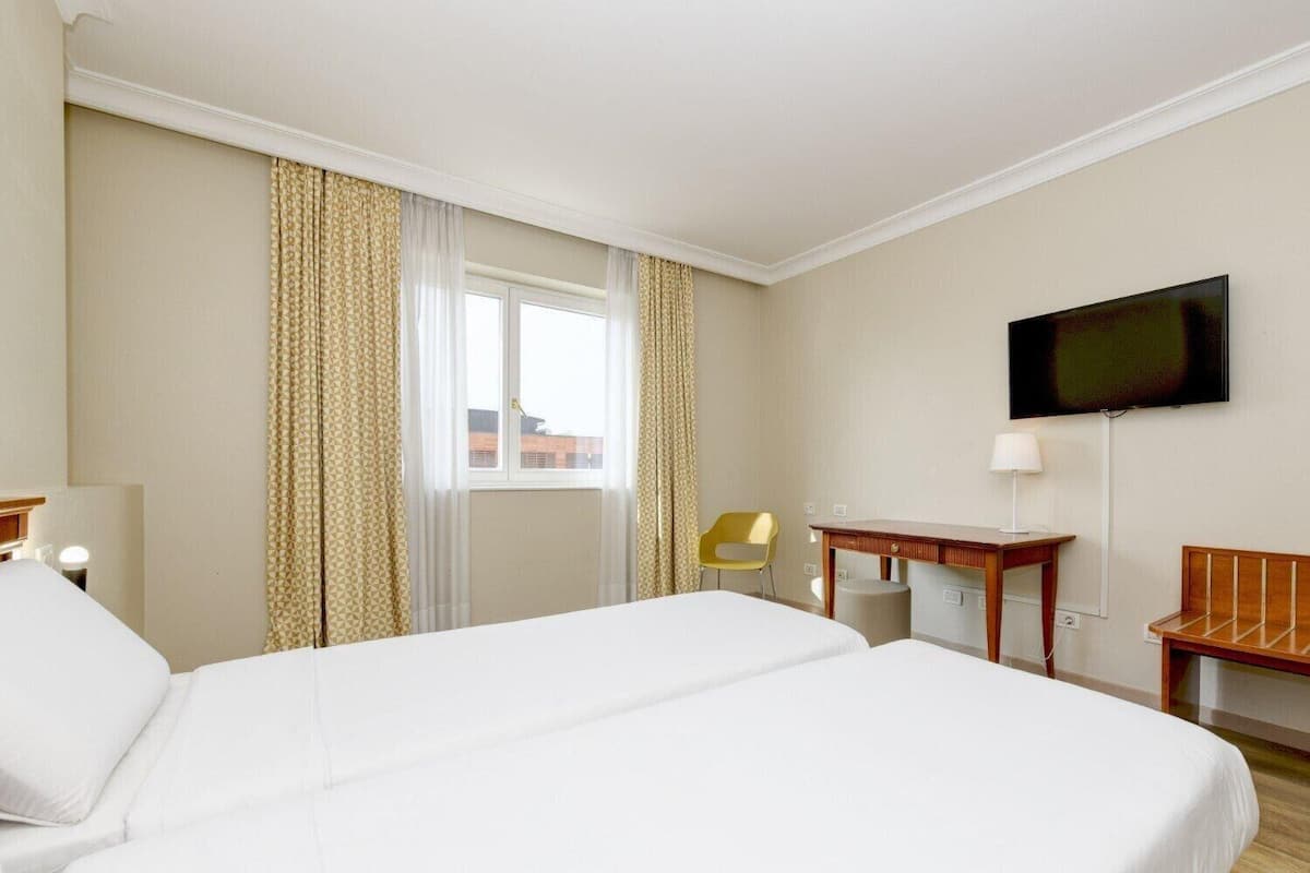 Une chambre d’hôtel avec un grand lit, un bureau, une chaise, une télévision et une fenêtre avec des rideaux.