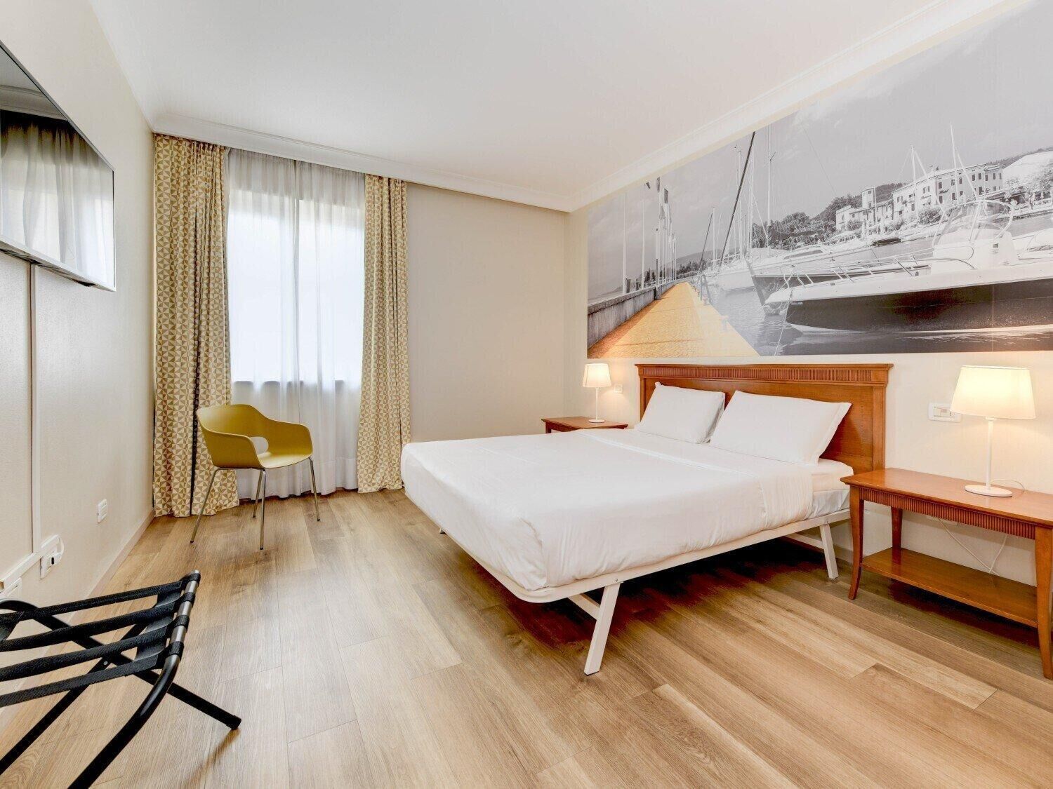 Une chambre d’hôtel avec un lit, une chaise, une table de chevet et un téléviseur fixé au mur.