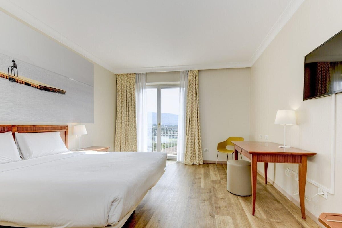 Une chambre d’hôtel avec un grand lit, une table de chevet en bois, une table, une chaise et un téléviseur fixé au mur.