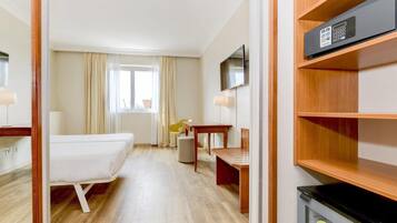 Ein Hotelzimmer mit Bett, Schreibtisch, Stuhl, Fernseher und einer Minibar.