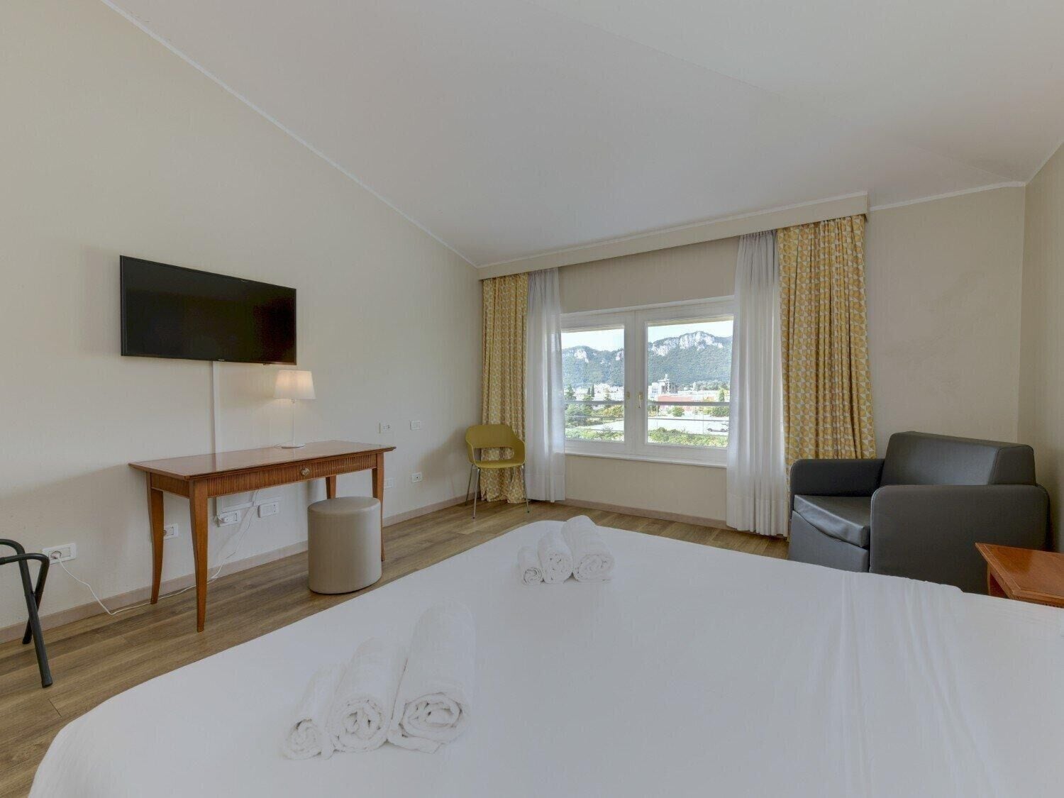 A hotel room with a bed, a desk, a chair, a TV, and a window with curtains.