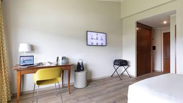 Habitación de hotel con cama, escritorio con computadora portátil, silla, mesita, cesto de basura y perchero.