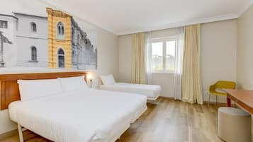 A hotel room with two beds, a wooden headboard, a desk, a chair, and a view of a building through the window.