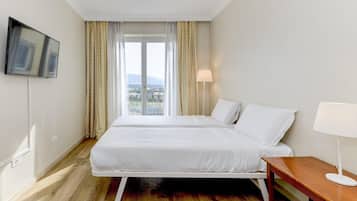 Une chambre d’hôtel avec un lit, une table de chevet, une lampe, un téléviseur fixé au mur et une fenêtre avec des rideaux.