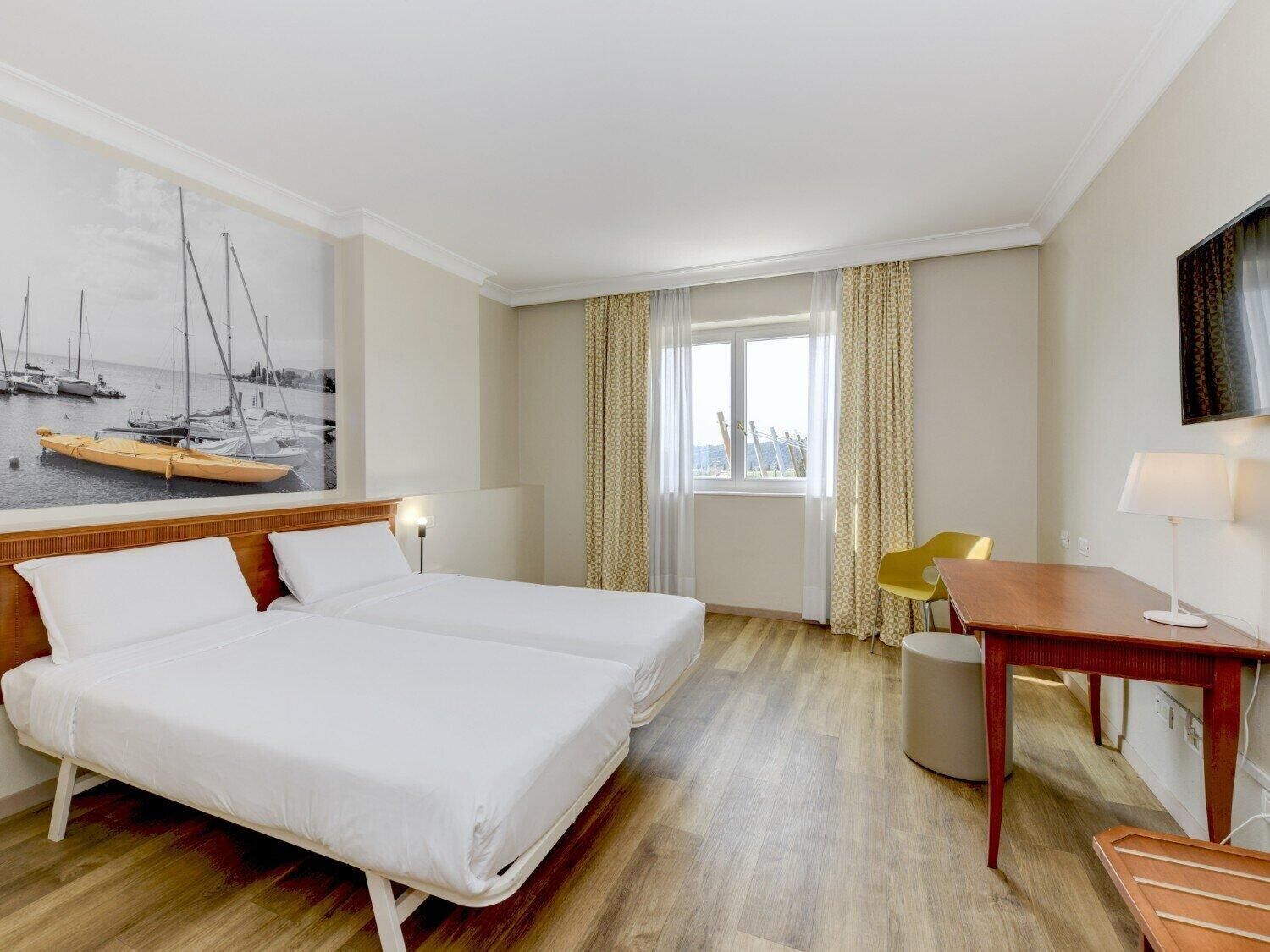 Una habitació d'hotel amb llit, escriptori, cadira, televisió i finestra amb cortines.