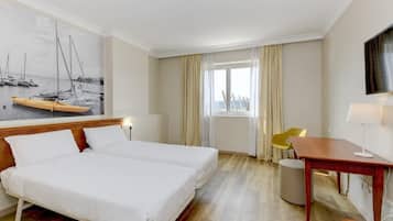 Una habitació d'hotel amb llit, escriptori, cadira, televisió i finestra amb cortines.