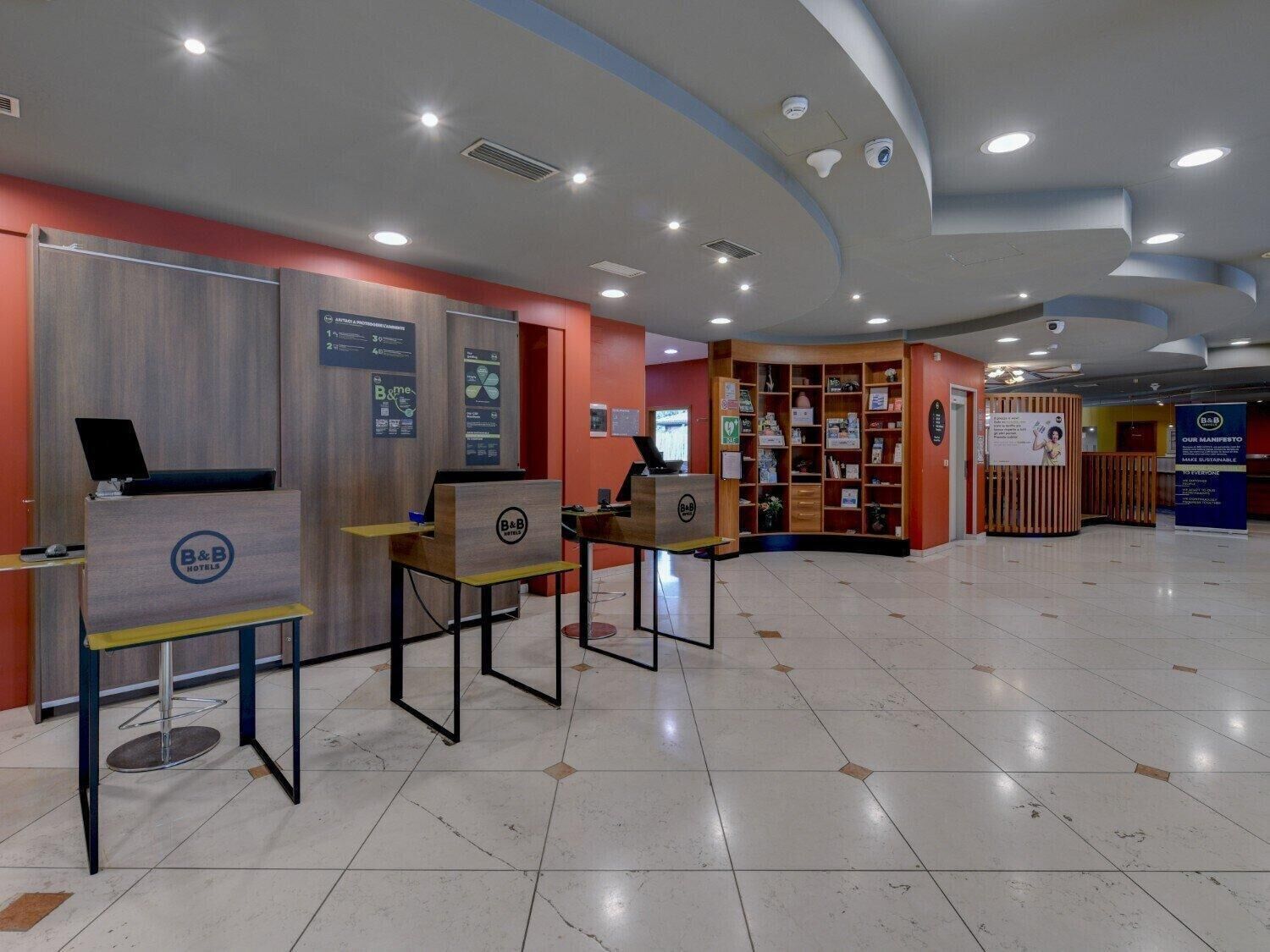 Un espace d’accueil d’hôtel au design moderne, comprenant un comptoir d’accueil, un coin salon et un présentoir de brochures et de documents d’information.