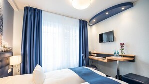 Une chambre d’hôtel avec un lit, un bureau, une télévision et une fenêtre avec des rideaux.