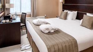 Habitación de hotel con cama, escritorio, silla, lámpara y ventana con cortinas.