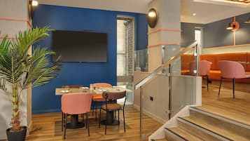 A modern dining area with a blue accent wall, a large potted plant, and a staircase leading to an upper level.