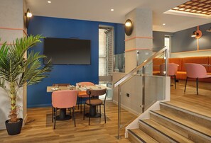 Un espace de repas moderne avec un mur d’accent bleu, une grande plante en pot et un escalier menant à un niveau supérieur.