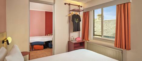 Una habitación de hotel con cama, armario, ventana con cortinas y vistas al exterior.