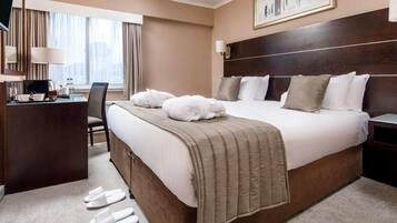 Habitación de hotel con una cama grande, un escritorio, una silla y una ventana con cortinas.