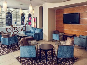 A hotel lobby with seating areas, a flat-screen TV mounted on a wooden panel, and a patterned carpet. - lyf George Square Glasgow (Glasgow)