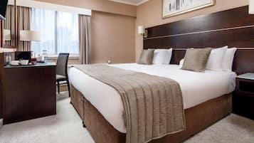 Habitación de hotel con una cama grande, un escritorio, una silla, un televisor y una ventana con cortinas.