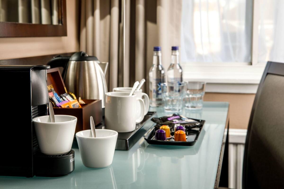 Une chambre d’hôtel équipée d’une kitchenette, comprenant une machine à café, des tasses, un plateau avec des condiments et une lampe.