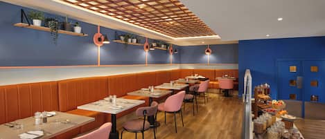 Un interior de restaurante moderno con paneles de madera, sillas rosadas y una variedad de plantas en estantes.