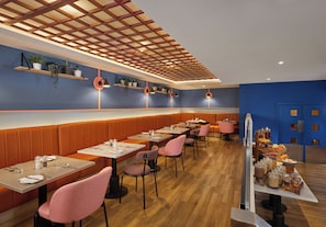 Ein modernes Restaurant-Interieur mit Holzvertäfelung, rosa Stühlen und verschiedenen Pflanzen auf Regalen.