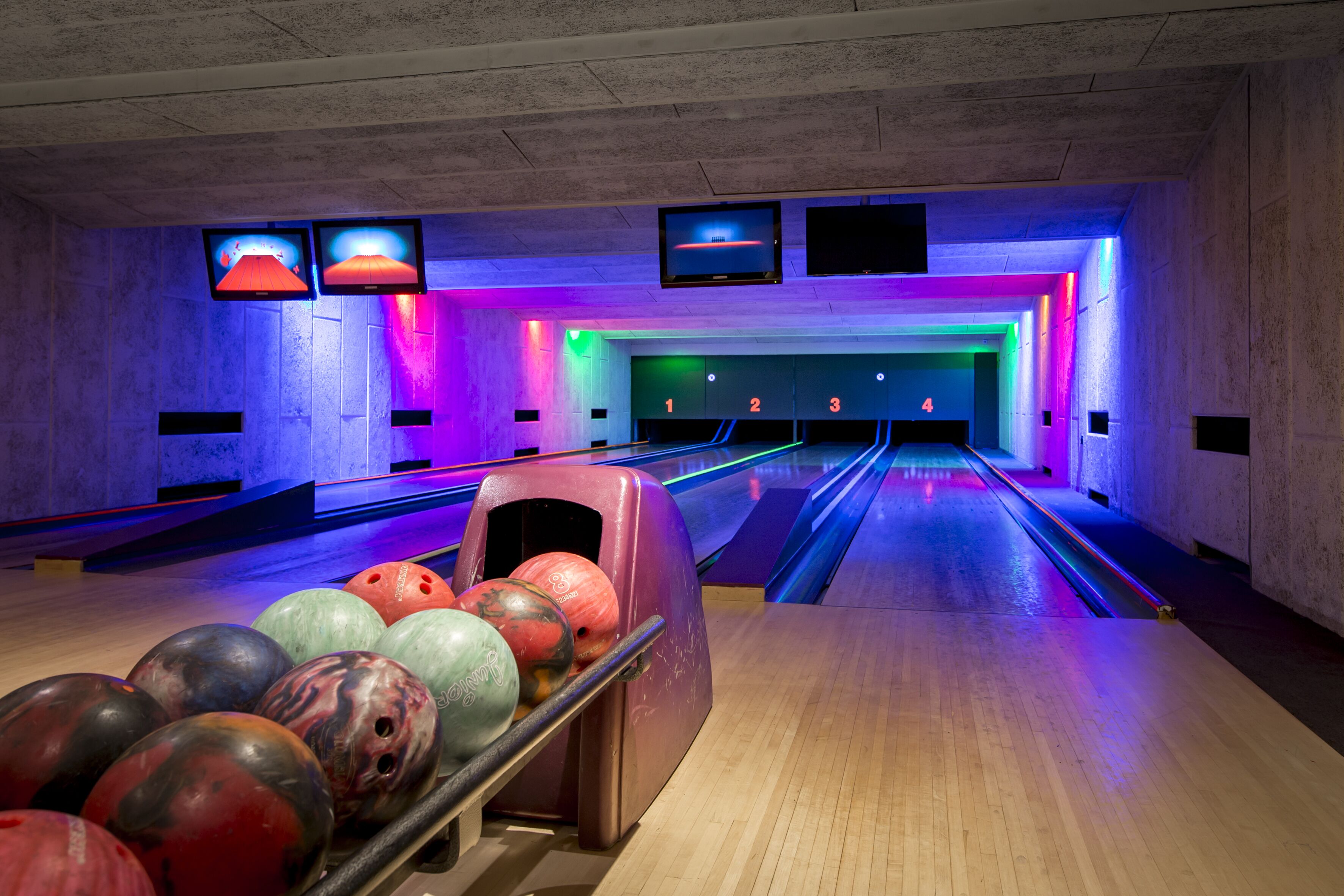 Una bolera con pistas, bolas de bolos y luces de neón.