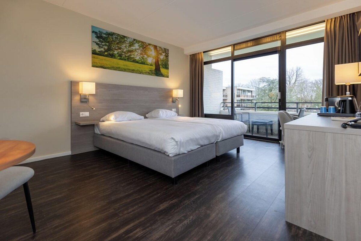 A modern hotel room with a large bed, a desk, and a view of the outdoors.