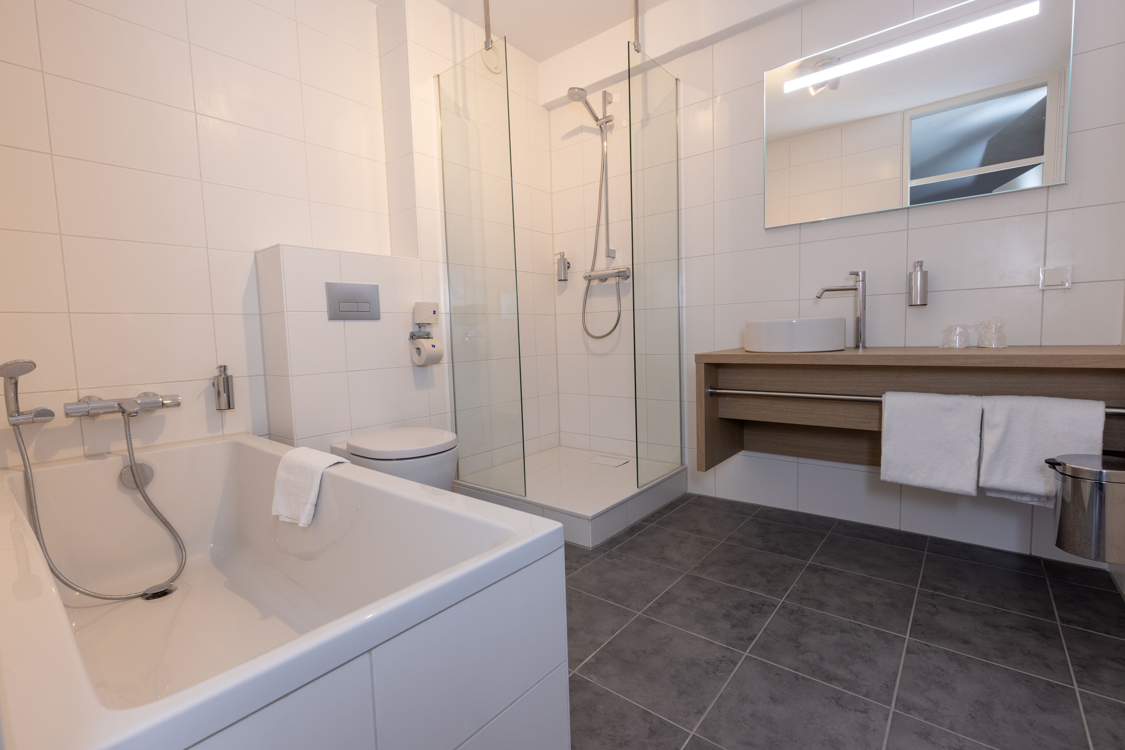 Un baño moderno con ducha de vidrio, bañera independiente, inodoro y tocador con espejo.