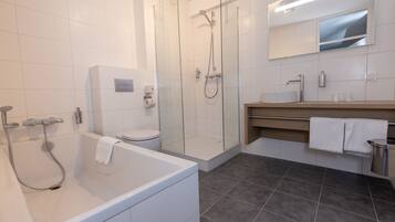Un baño moderno con ducha de vidrio, bañera independiente, inodoro y tocador con espejo.