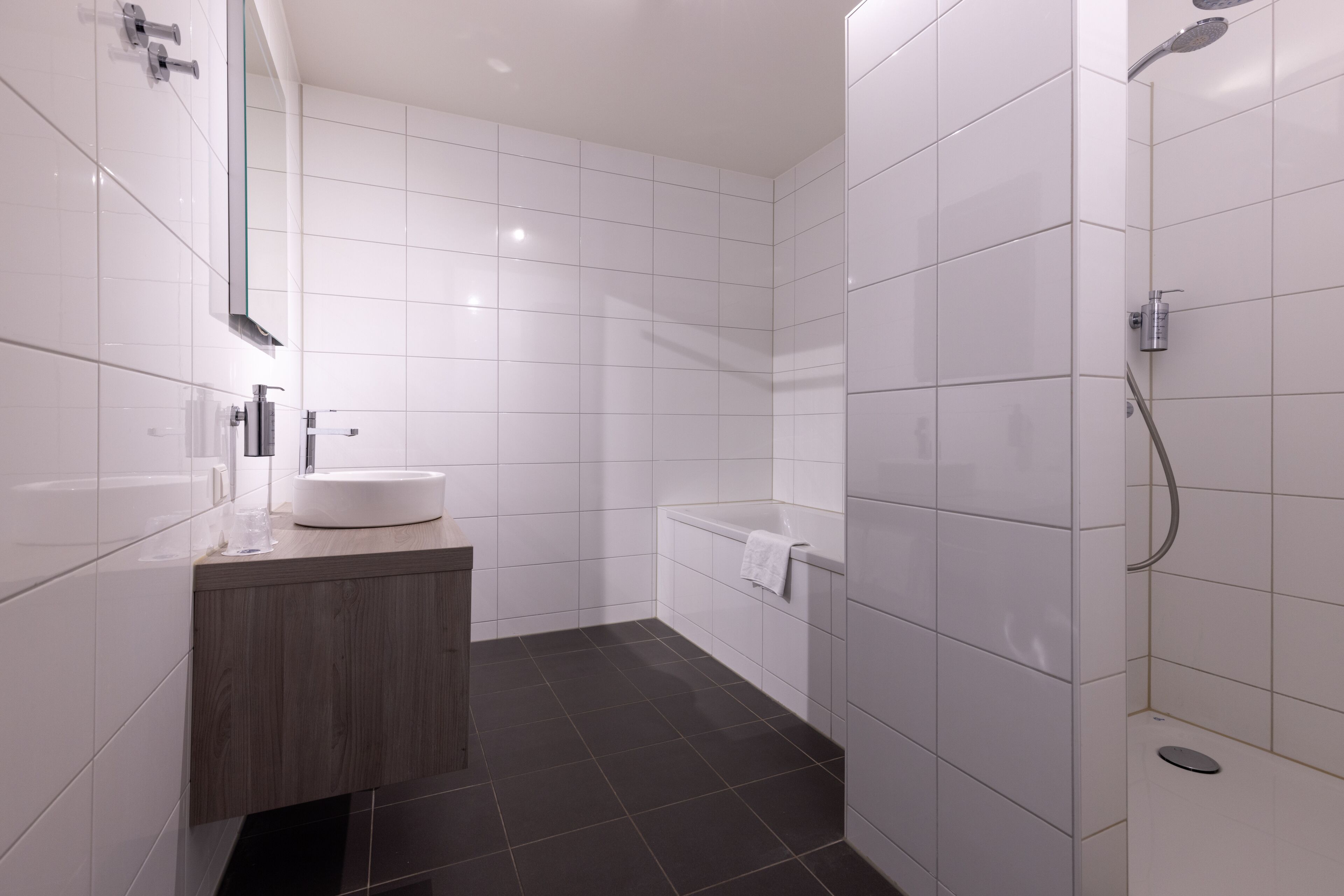 A modern bathroom with white tiles, a wooden vanity, a bathtub, and a shower.