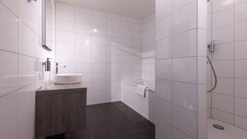A modern bathroom with white tiles, a wooden vanity, a bathtub, and a shower.