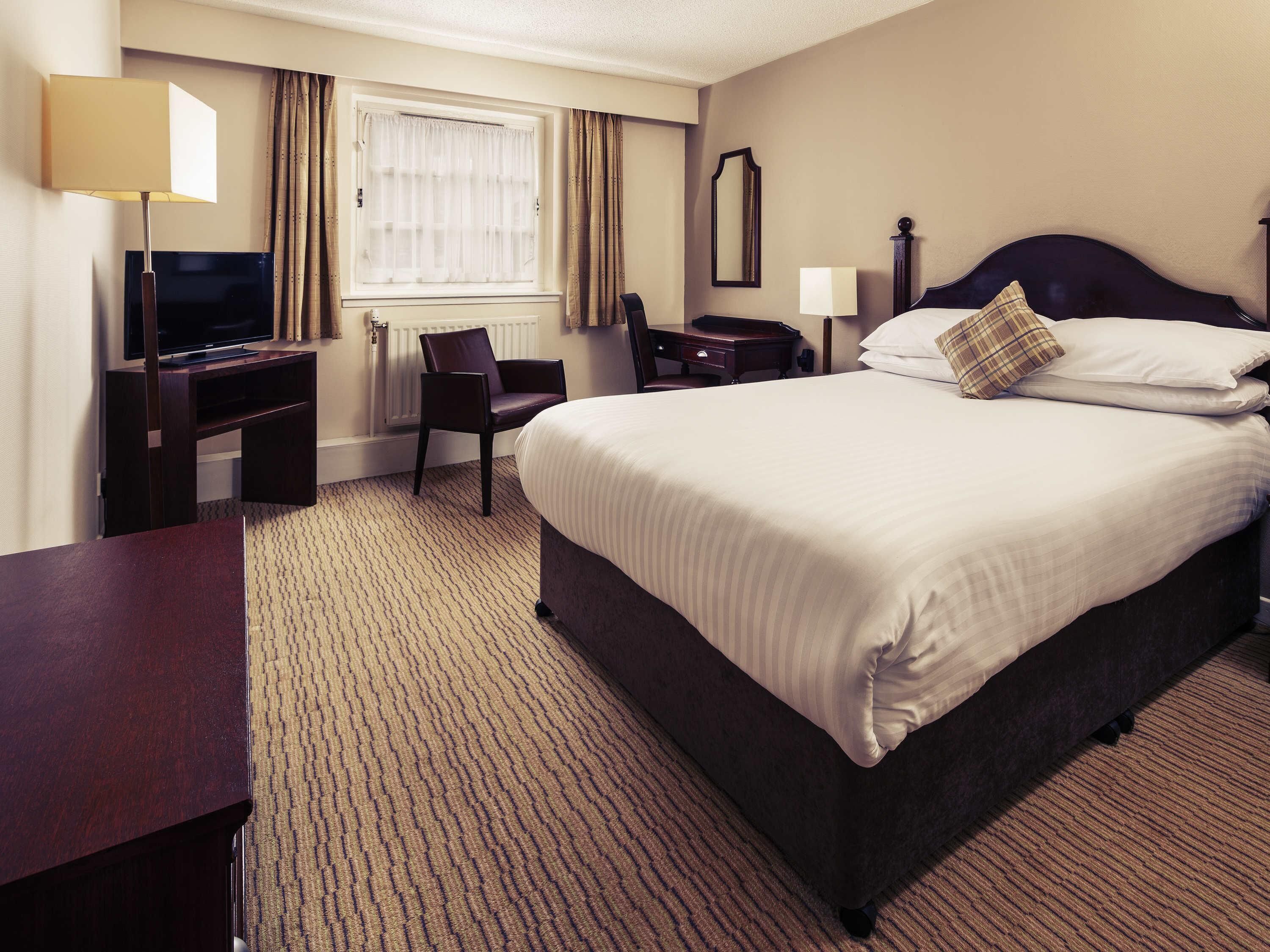 A hotel room with a bed, a desk, a chair, a television, and a window with curtains.