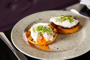 A plate with two poached eggs on toast, garnished with greens, on a speckled ceramic plate.