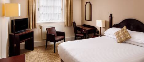 A hotel room with a large bed, a desk with a chair, a television, and a window with curtains.