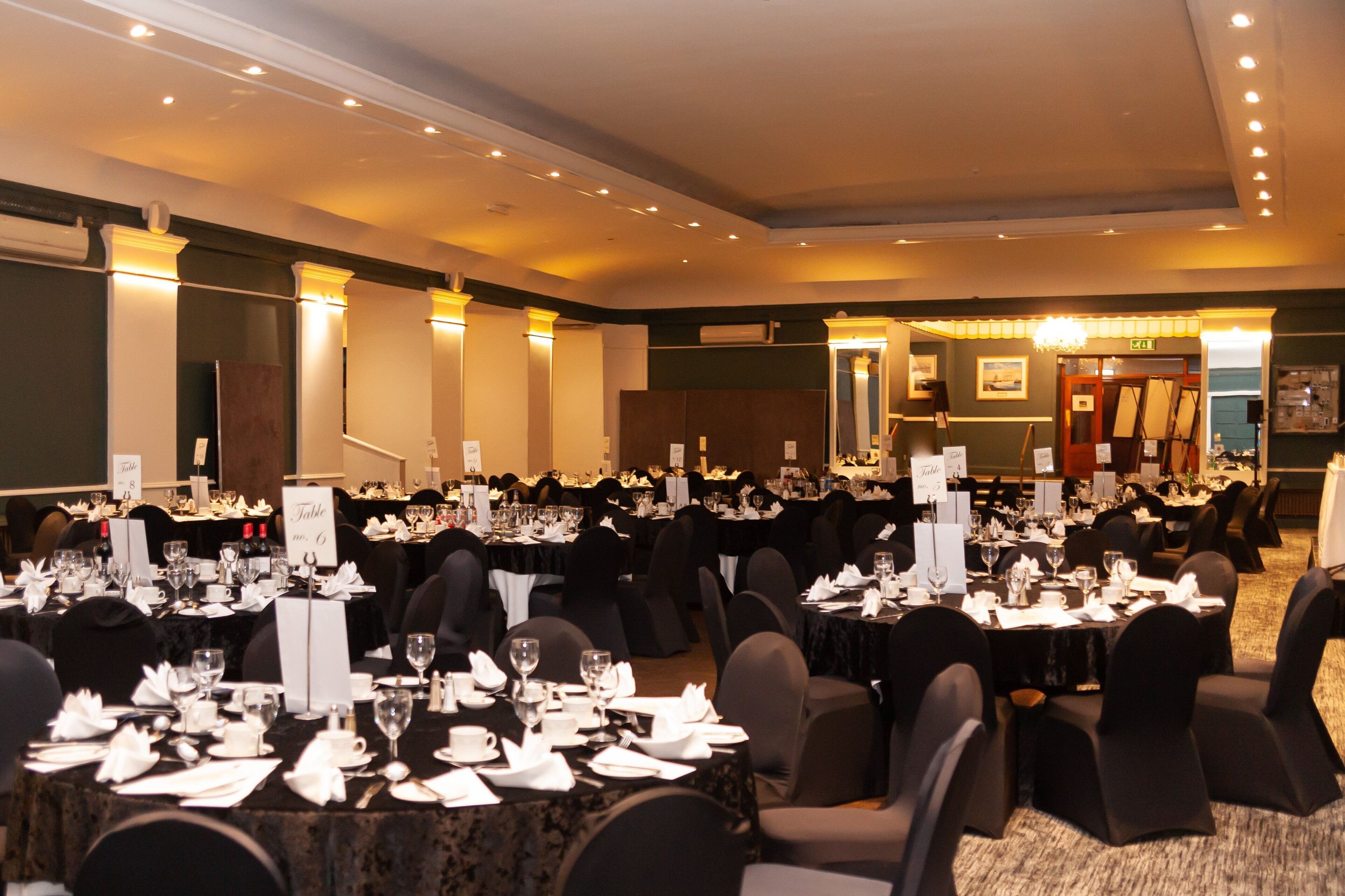 A banquet hall with multiple round tables set for dining, each with place settings and glassware.